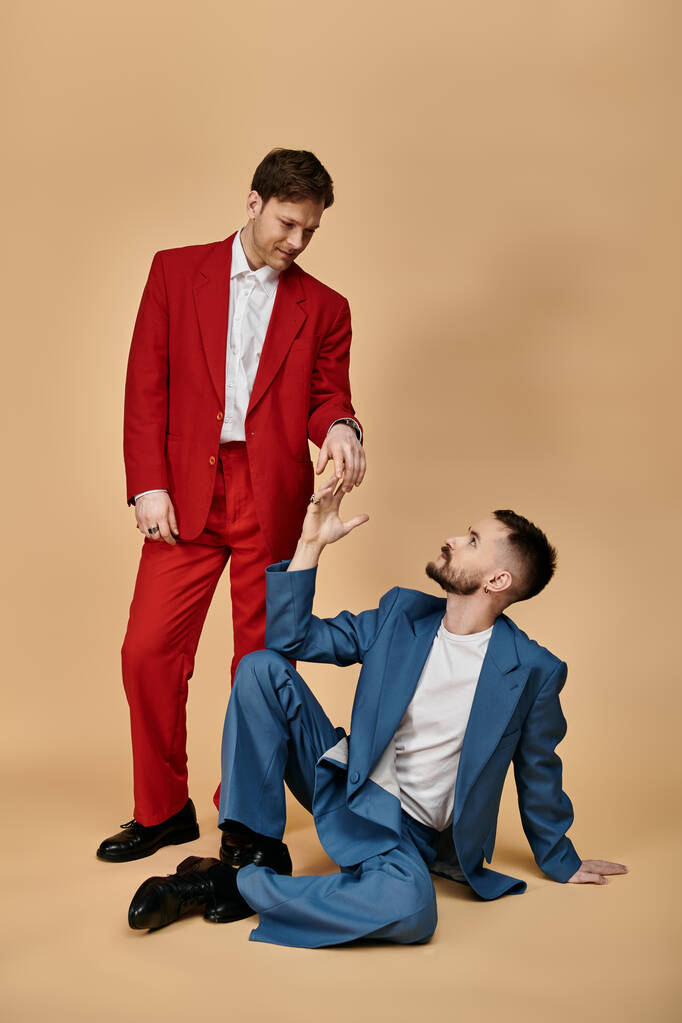 赤と青のスーツのゲイカップルは,柔らかく,笑い満ちた瞬間を共有しています. - 写真・画像