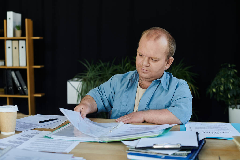 A man with inclusivity sits at a desk, diligently reviewing paperwork. - Photo, Image