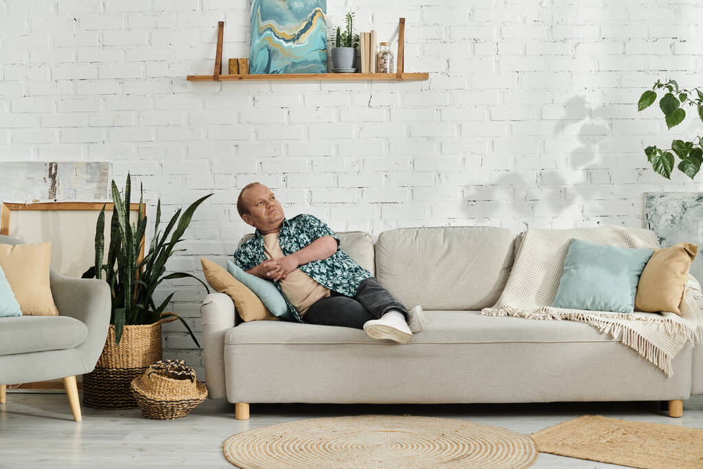 Mies, jolla on osallisuutta, makaa harmaalla sohvalla modernissa olohuoneessa. - Valokuva, kuva