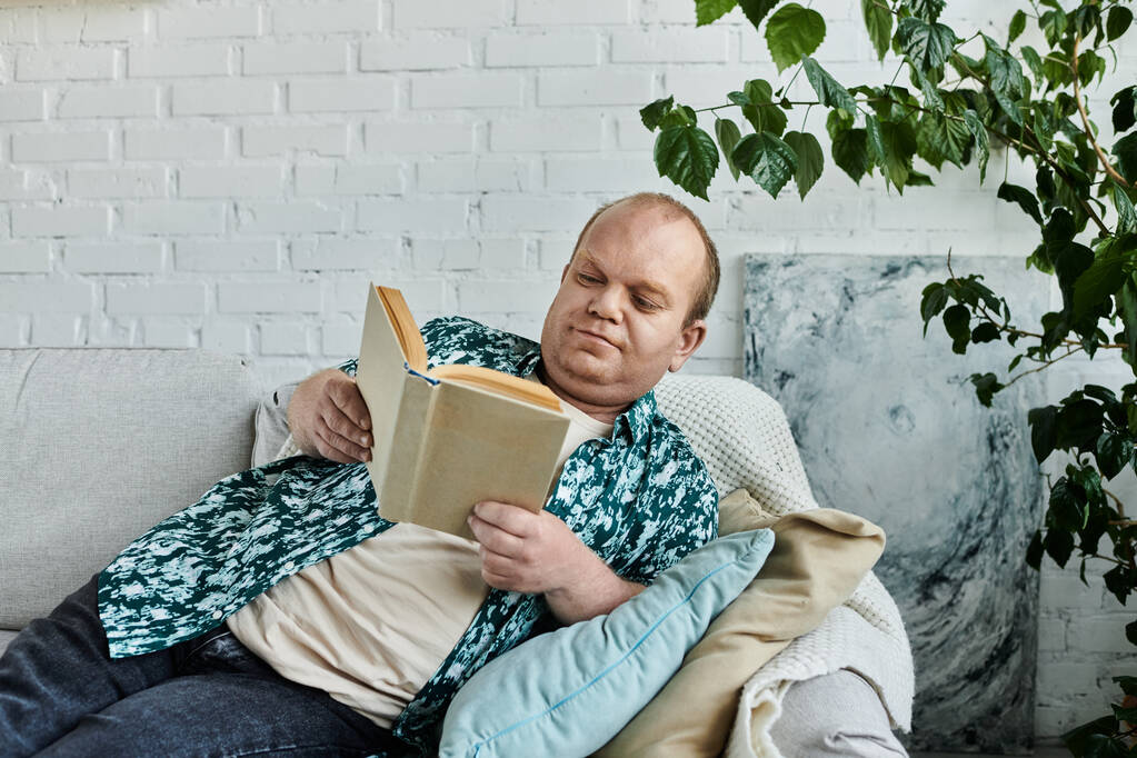 Muž s inkluzivitou odpočívá na gauči, pohlcen stránkami knihy. - Fotografie, Obrázek