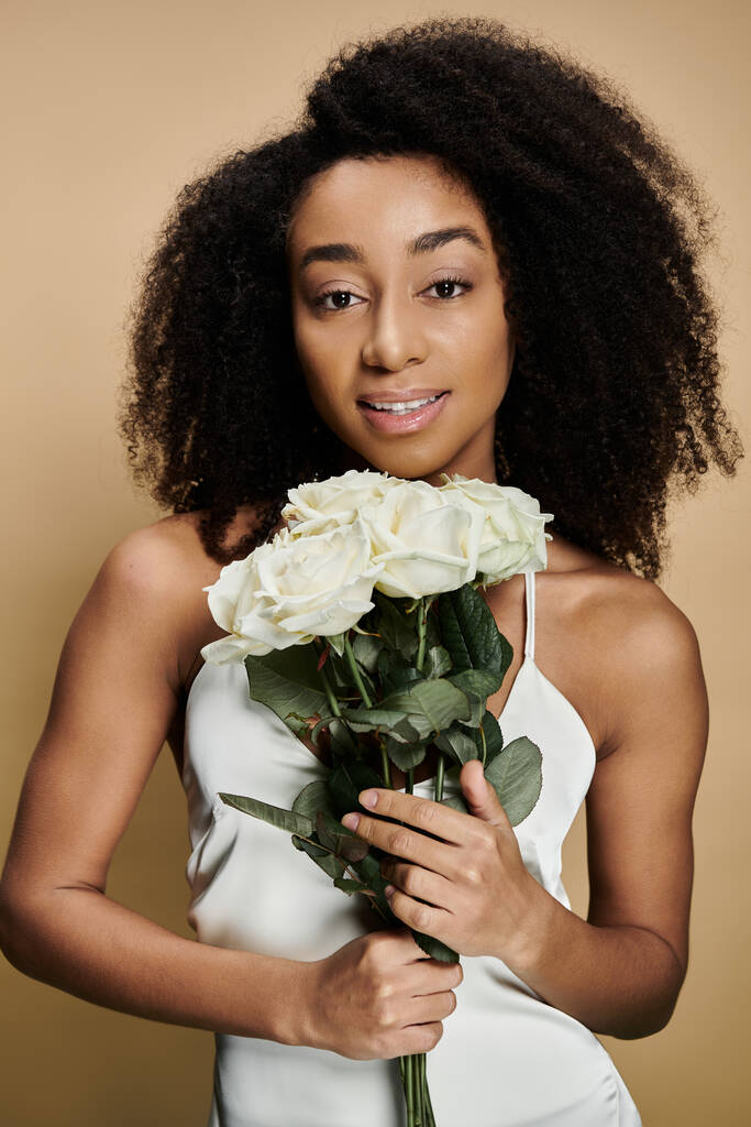 Portrét krásné Afroameričanky s přírodním make-upem držící kytici bílých květin na béžovém pozadí. - Fotografie, Obrázek