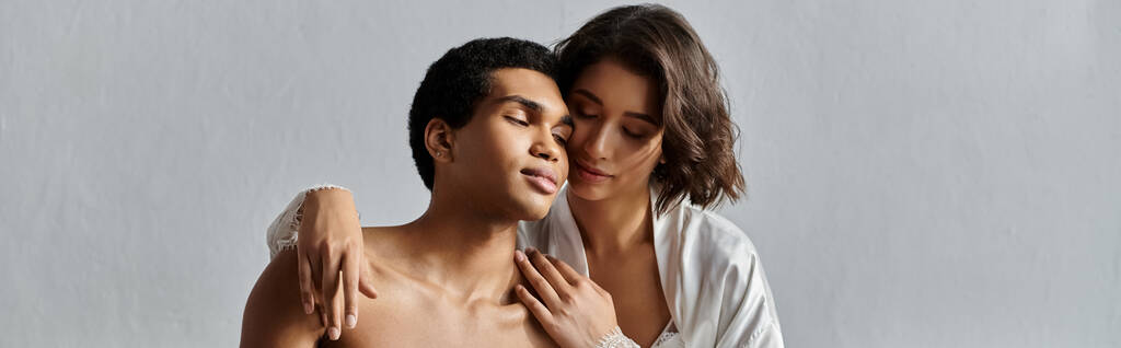 Una joven pareja multicultural se abraza en un tierno momento de intimidad, capturada en un acogedor entorno de dormitorio. - Foto, imagen