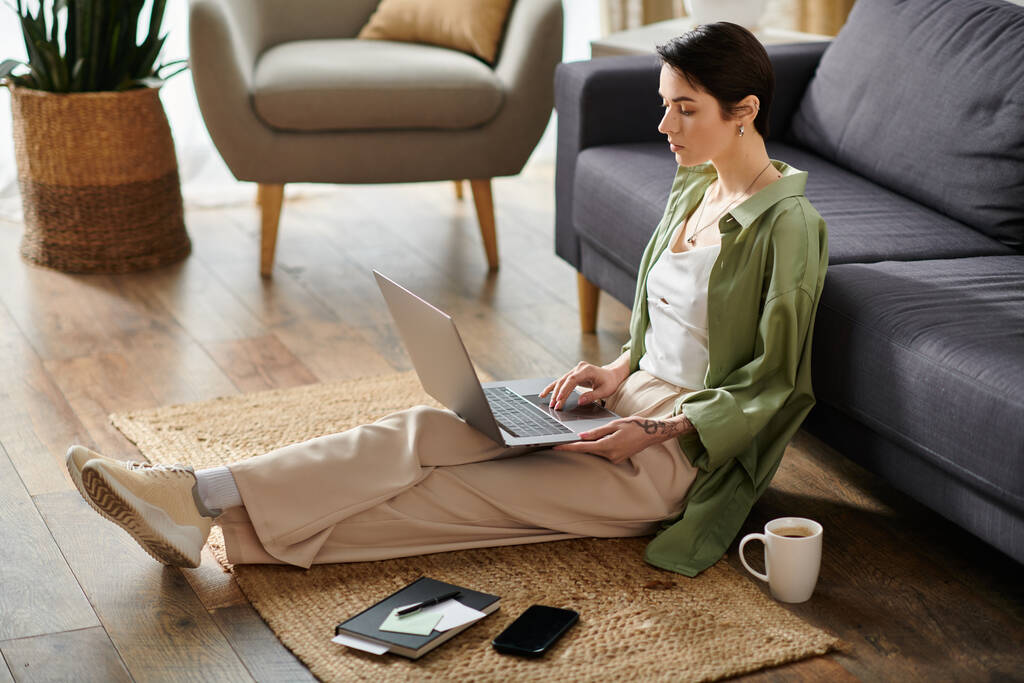 Une jolie femme est assise sur un tapis dans sa maison, travaillant sur son ordinateur portable. - Photo, image
