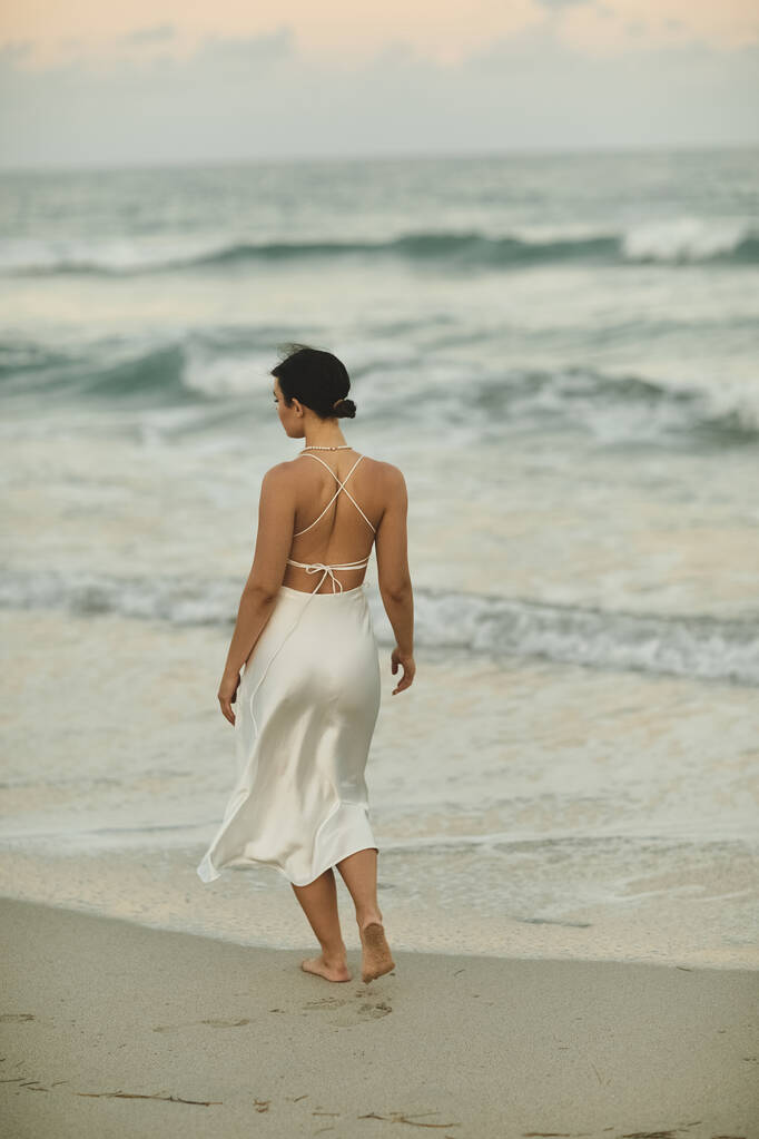 Молодая женщина в белом платье ходит босиком по песчаному пляжу в Майами. - Фото, изображение