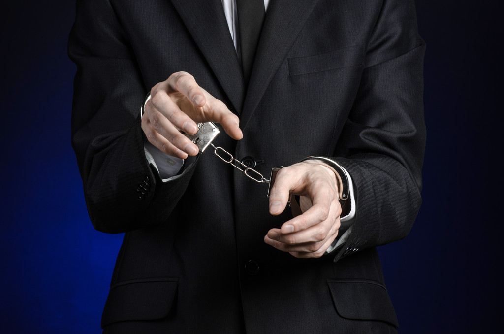 Korupce a úplatkářství téma: podnikatel v černém obleku s pouty na rukou na tmavě modrém pozadí ve studiu izolovaných - Fotografie, Obrázek