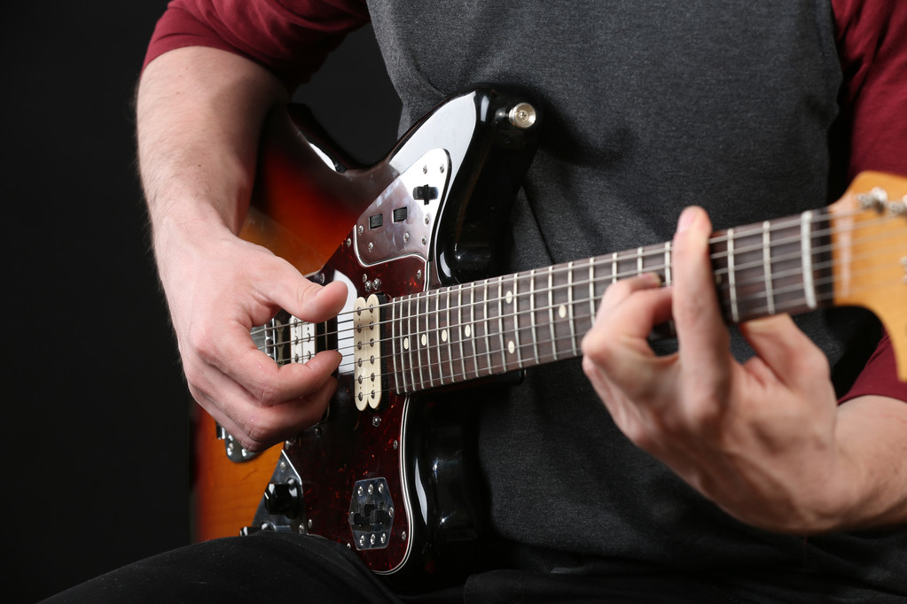 νεαρός άνδρας παίζει στην ηλεκτρική κιθάρα σε σκούρο φόντο - Φωτογραφία, εικόνα
