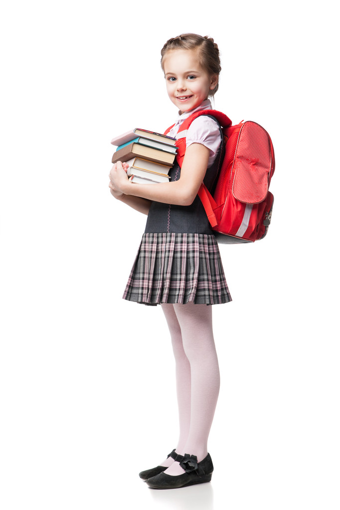 Χαριτωμένο χαμογελώντας μαθήτρια σε ομοιόμορφη στέκεται πάνω σε λευκό φόντο και κρατώντας τα βιβλία  - Φωτογραφία, εικόνα