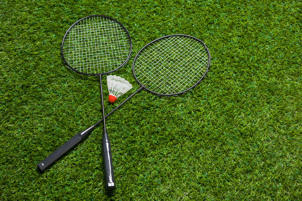 Перехрещені бадмінтонні ракетки лежать на траві
 - Фото, зображення