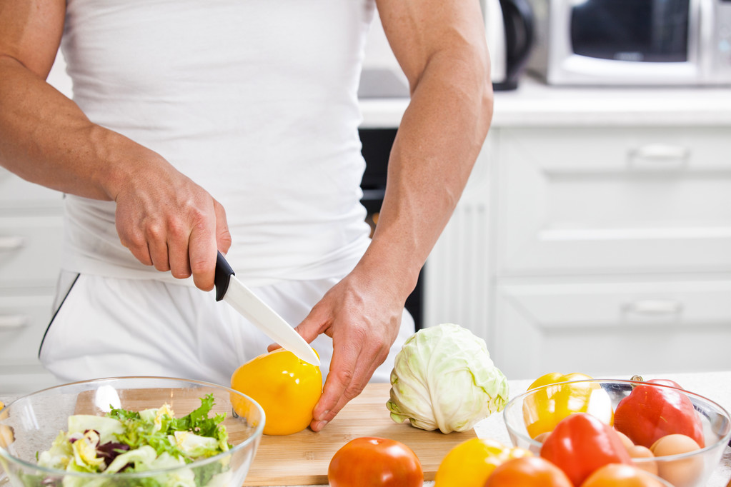 Schöner Mann kocht zu Hause und bereitet Salat in Küche zu. - Foto, Bild
