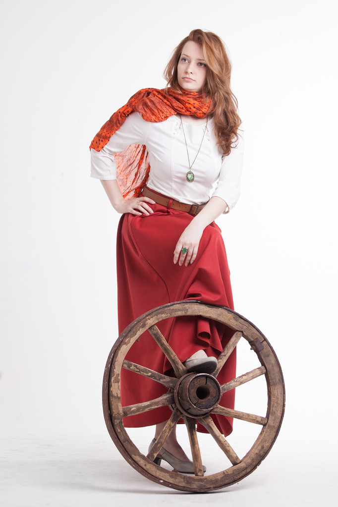 Mulher de saia vermelha longa de pé perto da roda do carrinho
 - Foto, Imagem