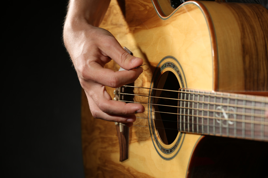 Молодой человек играет на акустической гитаре на темном фоне - Фото, изображение
