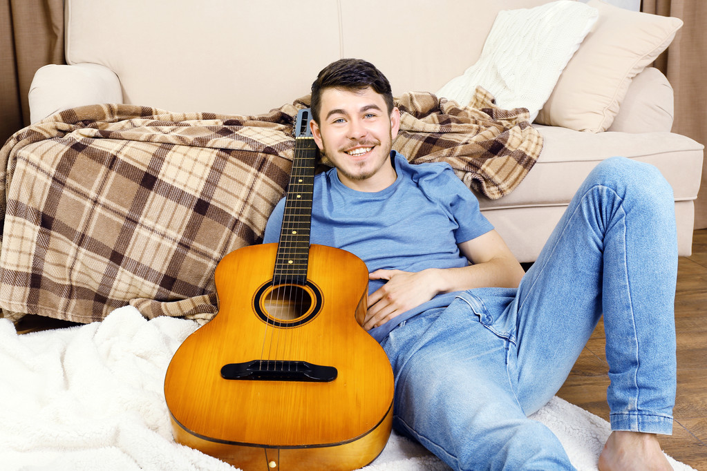 νεαρός άνδρας με κιθάρα στο πάτωμα στο δωμάτιο - Φωτογραφία, εικόνα