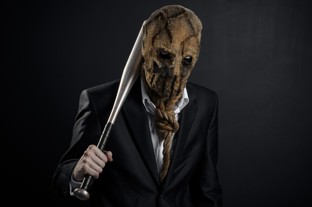 Fear and Halloween theme: a brutal killer in a mask holding a bat on a dark background in the studio - Φωτογραφία, εικόνα