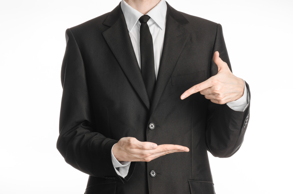 Businessman and gesture topic: a man in a black suit with a tie shows the left hand index finger on his right hand on a white isolated background in studio - Photo, Image