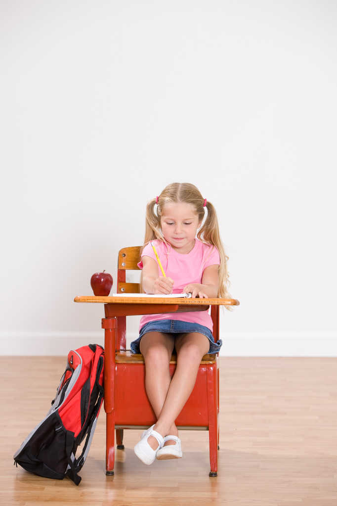 Школа: маленькая девочка-студентка сидит за партой, делая домашнюю работу
 - Фото, изображение