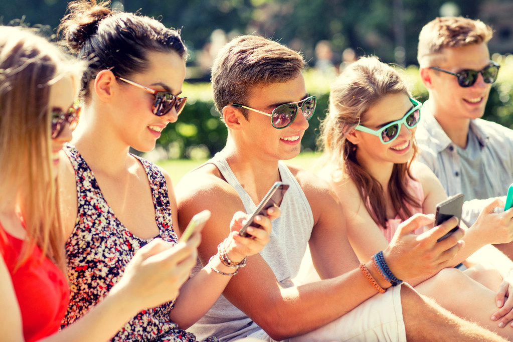 uśmiechnięty znajomych ze smartfonów, siedząc na trawie - Zdjęcie, obraz