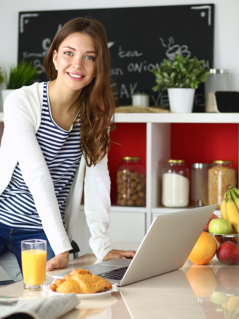 Attractive young woman using laptop and sitting in the kitchen  - Photo, Image