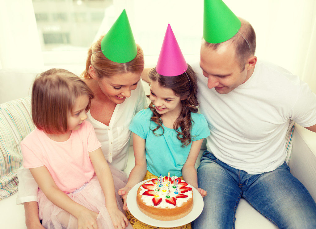 Famiglia sorridente con due bambini in cappelli con torta
 - Foto, immagini