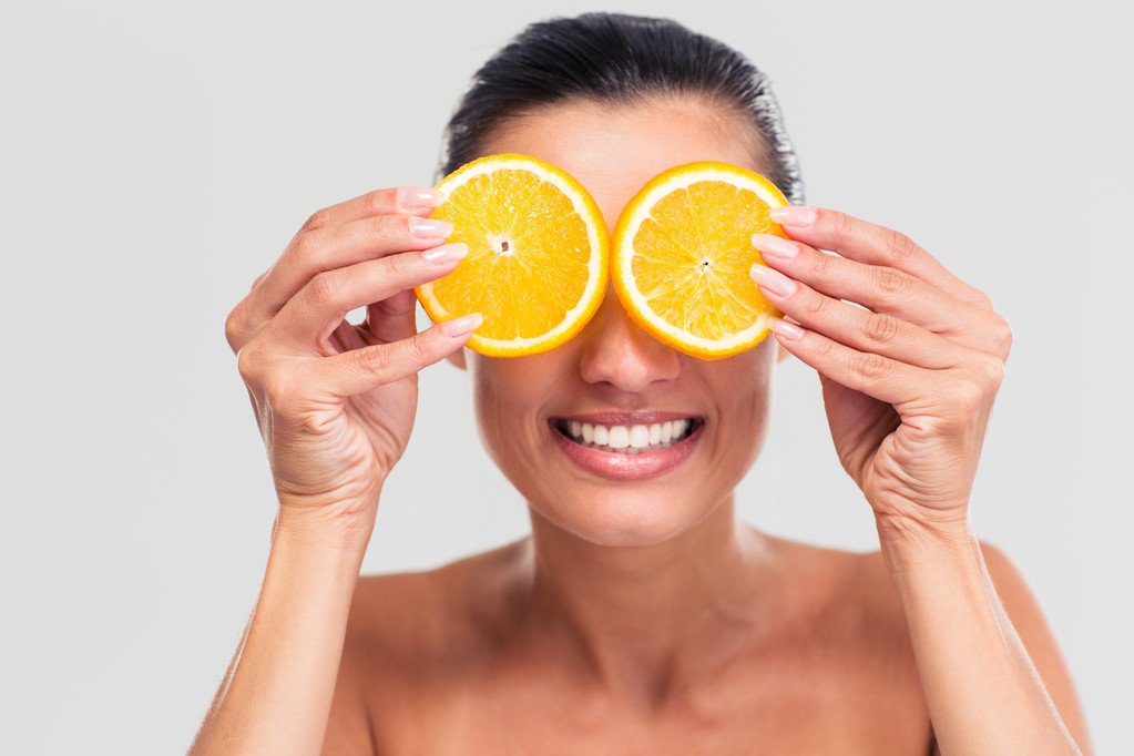 Smiling woman covering her eyes with orange - 写真・画像