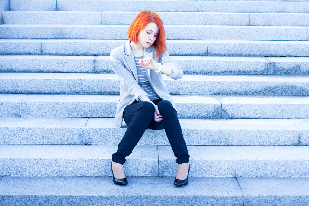 Pelirroja atractiva mujer sentada fuera en las escaleras y viendo el tiempo
 - Foto, Imagen