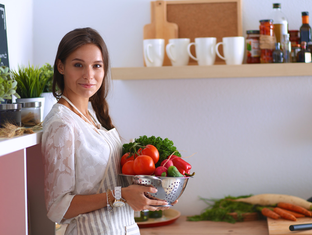 Усміхнена молода жінка тримає овочі, що стоять на кухні
 - Фото, зображення
