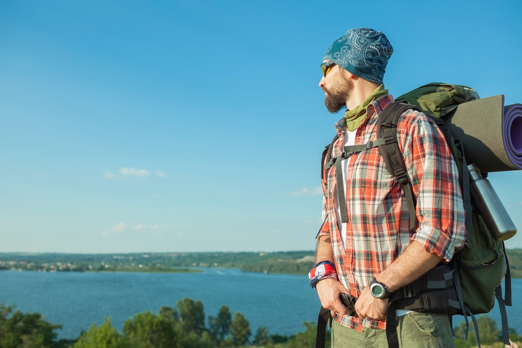 Junger kaukasischer Mann mit Rucksack steht auf dem Gipfel des Hügels - Foto, Bild