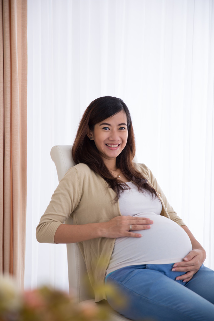Happy pregnant asian woman touching her big belly while sitting - Fotografie, Obrázek