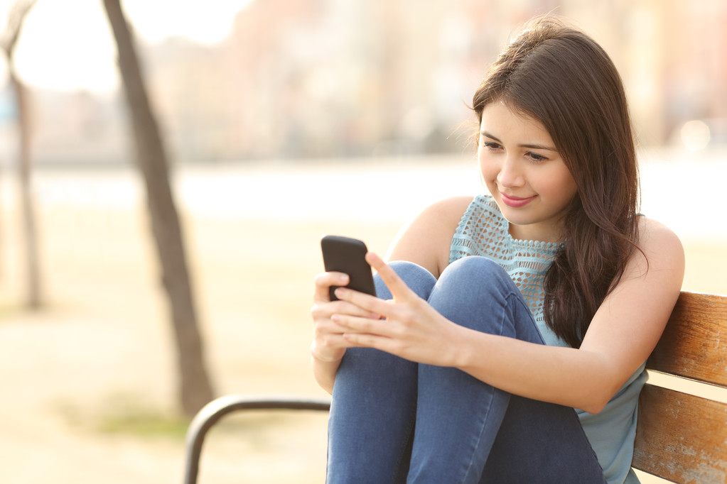 Έφηβος κορίτσι με ένα έξυπνο τηλέφωνο που κάθεται σε ένα παγκάκι - Φωτογραφία, εικόνα