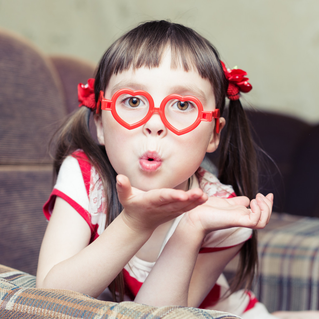Schattig klein meisje met bril in de vorm van een hart stuurt een lucht-kus - Foto, afbeelding