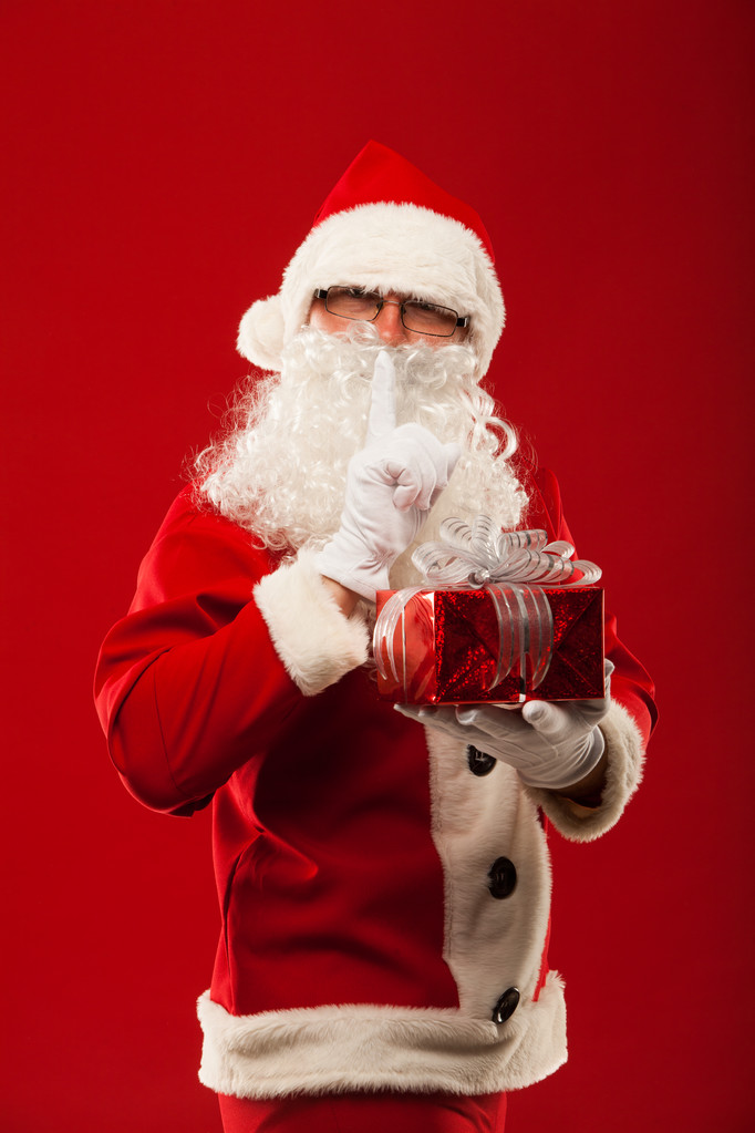 Fotografie z druhu Santa Claus dávat vánoční dárek a při pohledu na fotoaparát. tajné rukou rty. - Fotografie, Obrázek