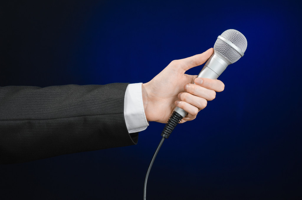 Geschäfts- und Redethema: Mann im schwarzen Anzug mit Mikrofon auf grauem dunkelblauem Hintergrund im Studio - Foto, Bild