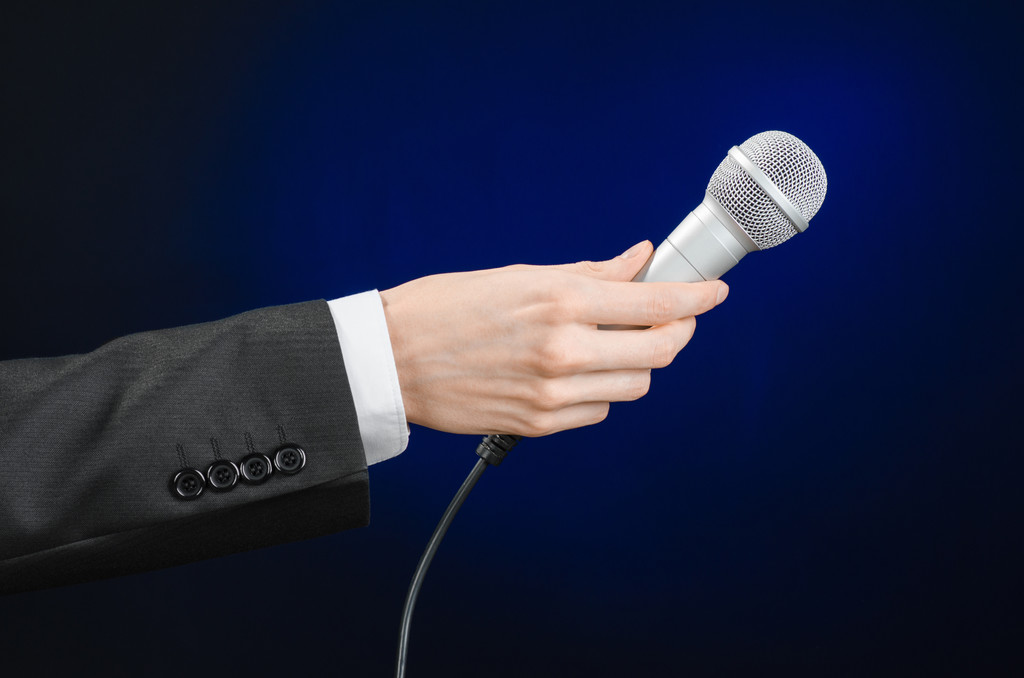 Tópico de negócios e discurso: Homem de terno preto segurando um microfone em um fundo azul escuro cinza isolado em estúdio
 - Foto, Imagem