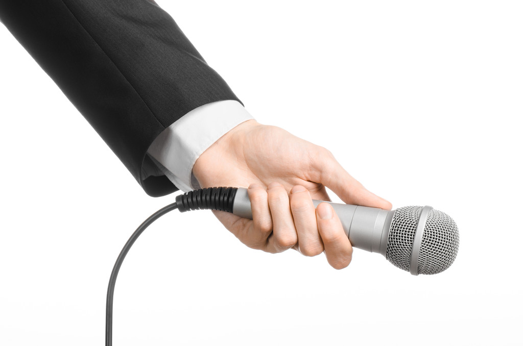 Business en spraak onderwerp: Man in zwart pak houden een grijze microfoon op een afgelegen witte achtergrond in studio - Foto, afbeelding