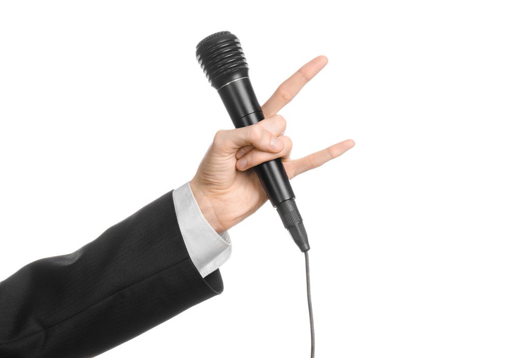 Argomento Affari e discorso: Uomo in tuta nera con un microfono nero isolato su sfondo bianco in studio
 - Foto, immagini