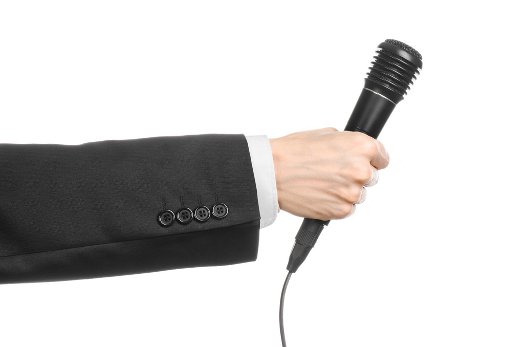 Geschäfts- und Redethema: Mann im schwarzen Anzug hält ein schwarzes Mikrofon isoliert auf weißem Hintergrund im Studio - Foto, Bild