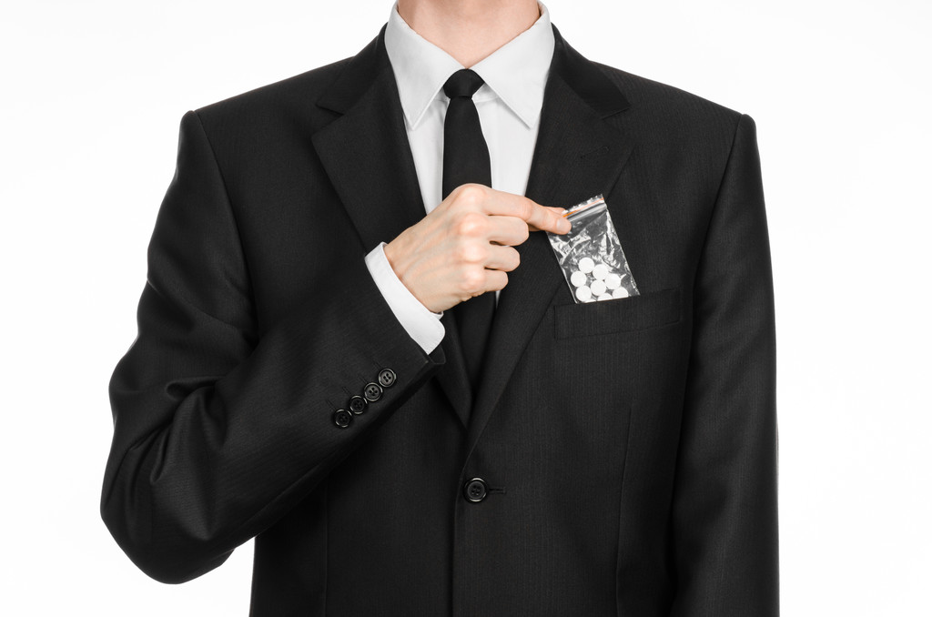 Addiction and business topic: hand in a black suit holds bag with white pills a drug on a white isolated background in studio - 写真・画像