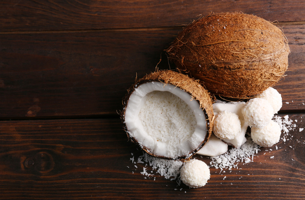 Snoepjes in kokosnoot vlokken en verse kokosnoot op donkere houten achtergrond - Foto, afbeelding