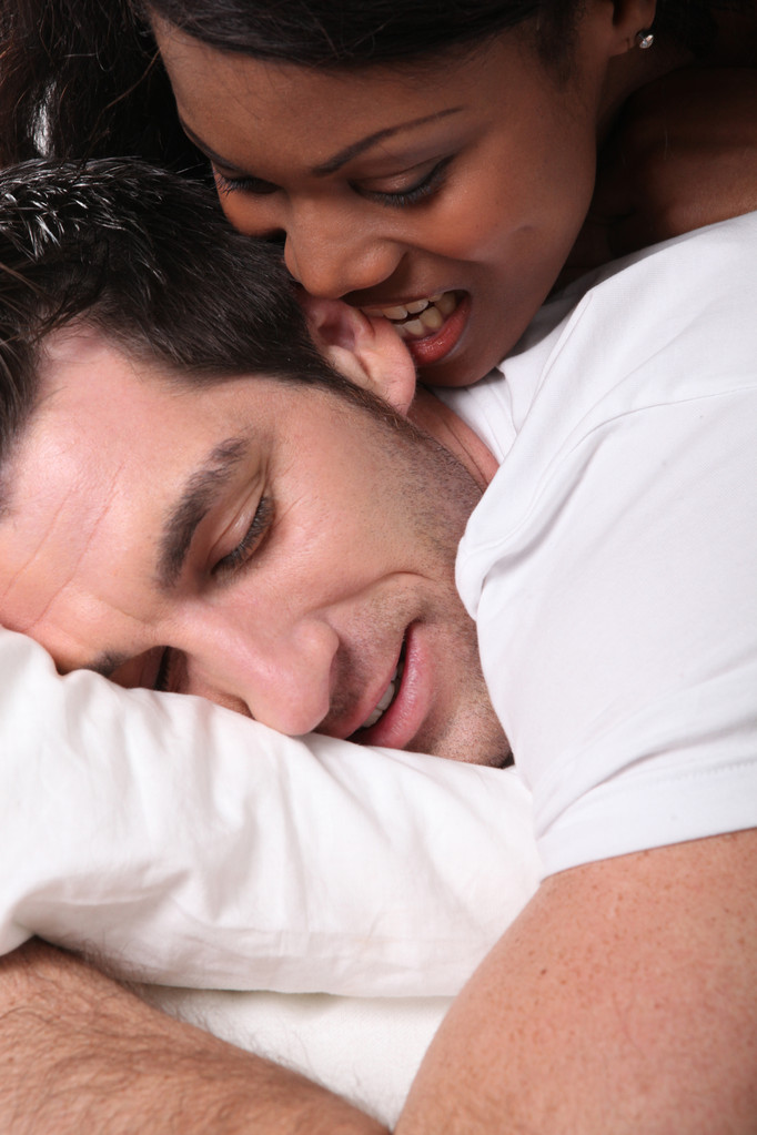Nainen puree miehensä korvaa sängyssä
 - Valokuva, kuva