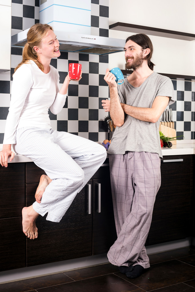 nuori onnellinen hymyilevä valkoihoinen pari keittiössä juo aamukahvia ja puhuu toisilleen
 - Valokuva, kuva