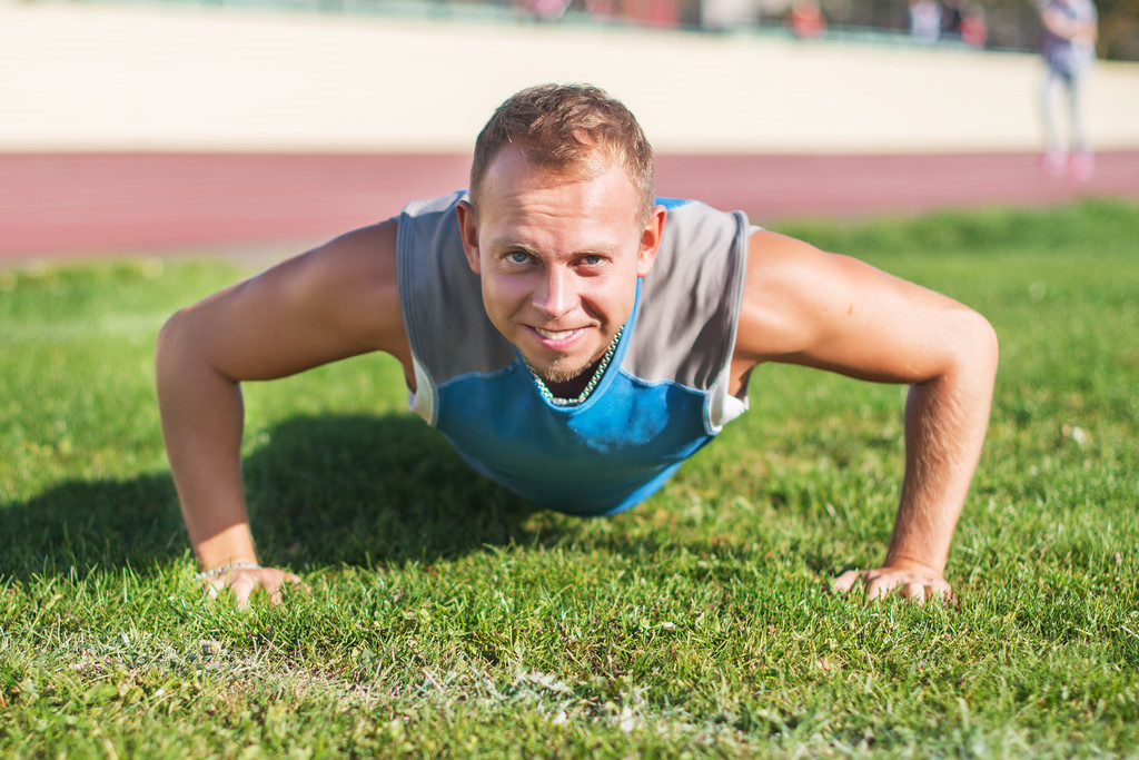 Sport férfi a nyújtás, a park, csinál fekvőtámaszokat a fűben, egy napsütéses napon. Fitness fogalmak. - Fotó, kép