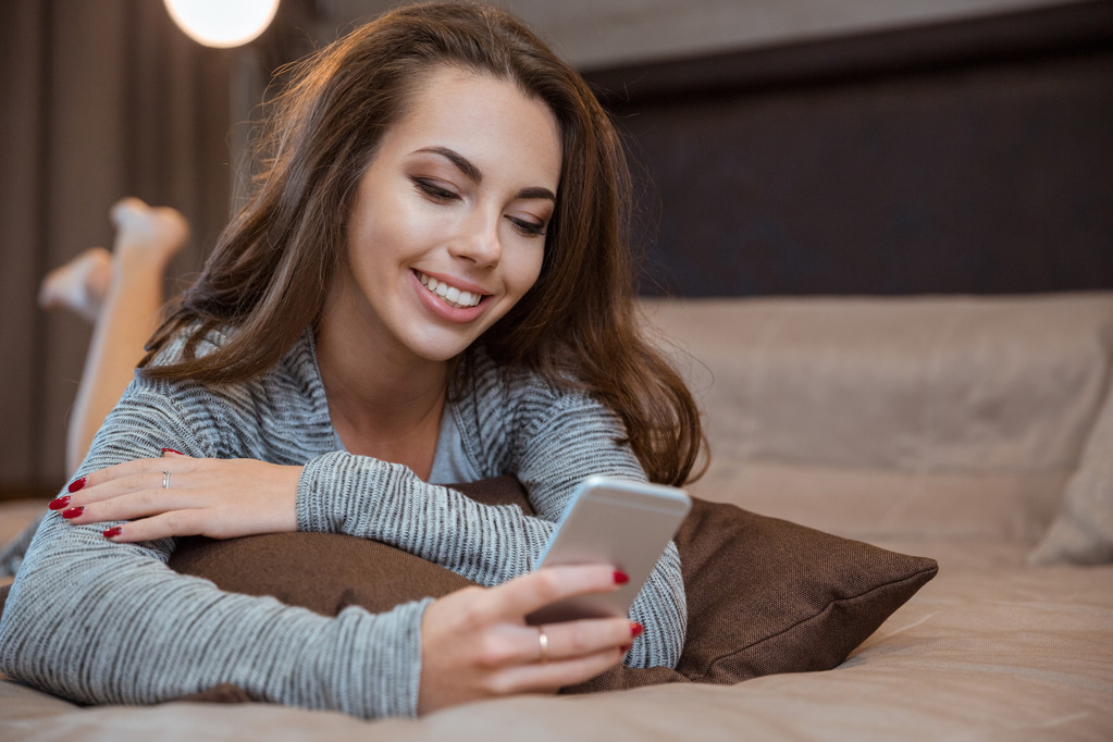 Frau liegt auf dem Bett und benutzt Smartphone - Foto, Bild