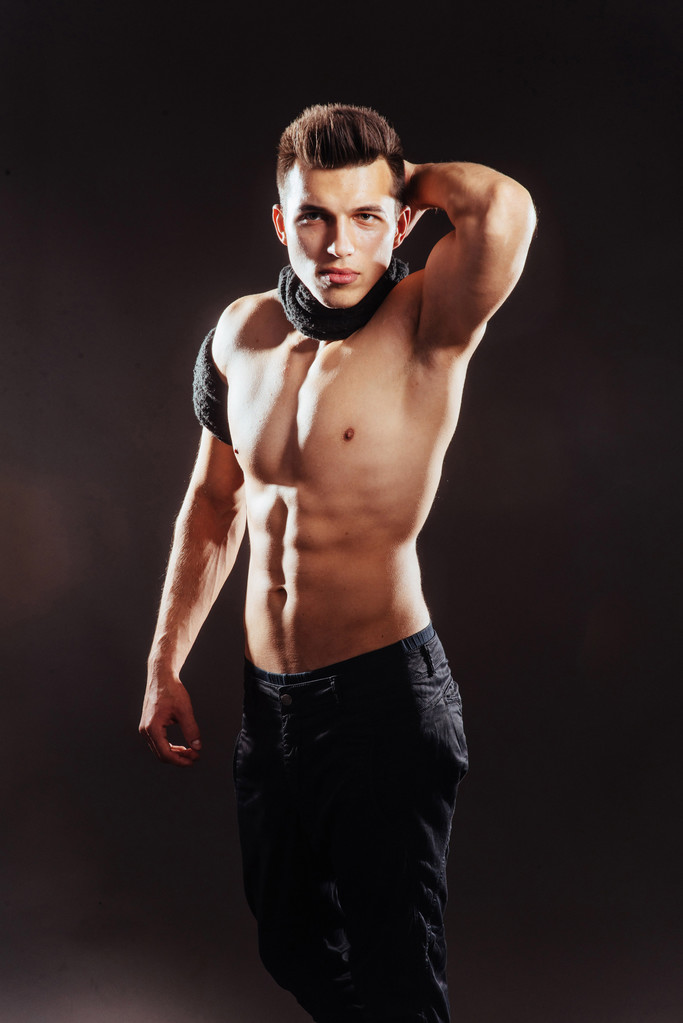 sexy junger Mann mit nacktem Oberkörper auf dunklem Hintergrund  - Foto, Bild
