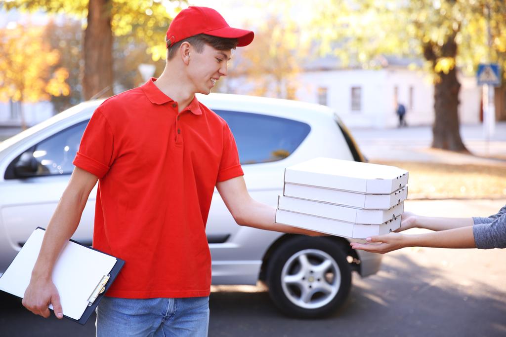 Хлопчик з доставкою піци тримає коробки з піцою біля автомобіля
 - Фото, зображення