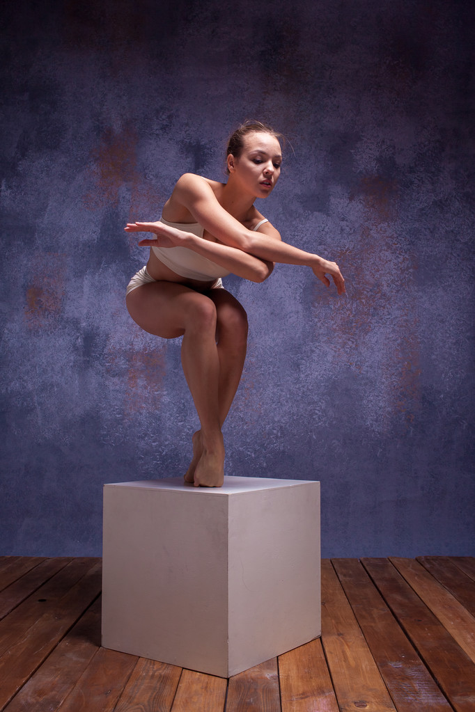 Молода красива танцівниця в бежевому купальнику позує на білому кубі
 - Фото, зображення
