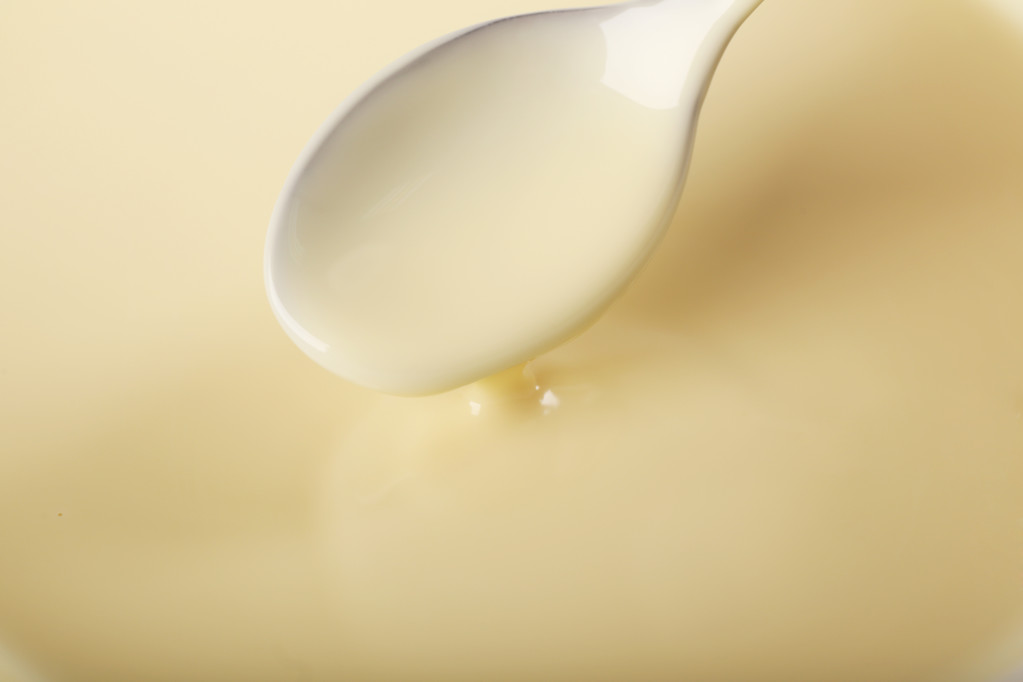 Fundo de leite condensado e uma colher em uma tigela, close-up
 - Foto, Imagem