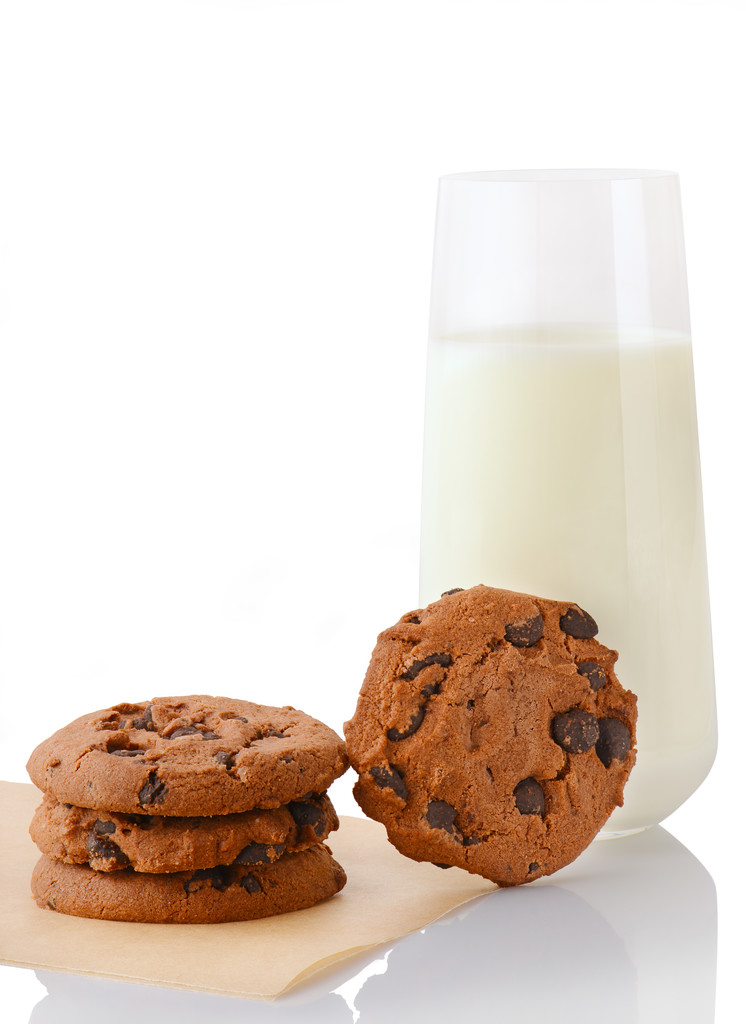 Tři domácí čokoláda čip cookies na pečící papír, jediného souboru cookie a sklenice mléka - Fotografie, Obrázek