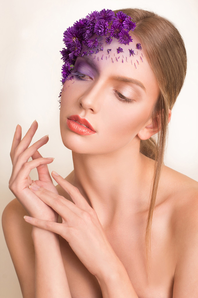 Retrato de una joven hermosa chica fresca con un maquillaje elegante y flores púrpuras alrededor de su cara y cabello
. - Foto, imagen