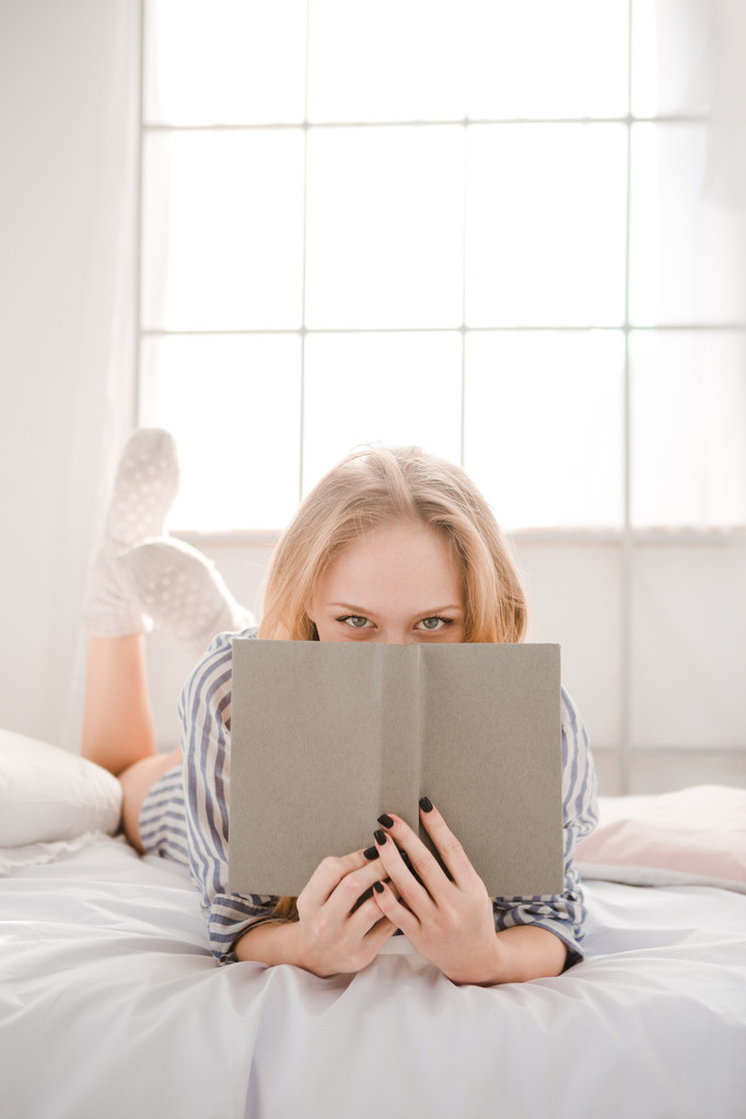 Игривая девушка, прячущая лицо за книгой
  - Фото, изображение