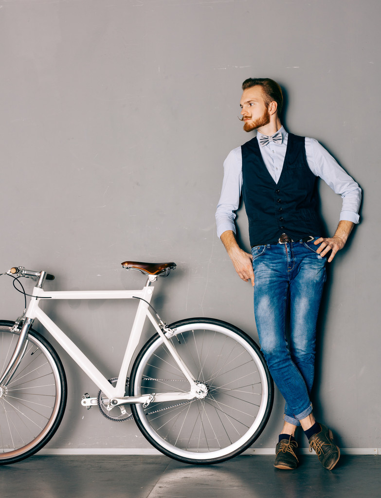 Bıyık ve sakal genç bir adamla şık modern fixgear bisiklet olduğunu. Kot pantolon ve gömlek, yelek ve papyon hippi tarzı. Tonlu renk - Fotoğraf, Görsel