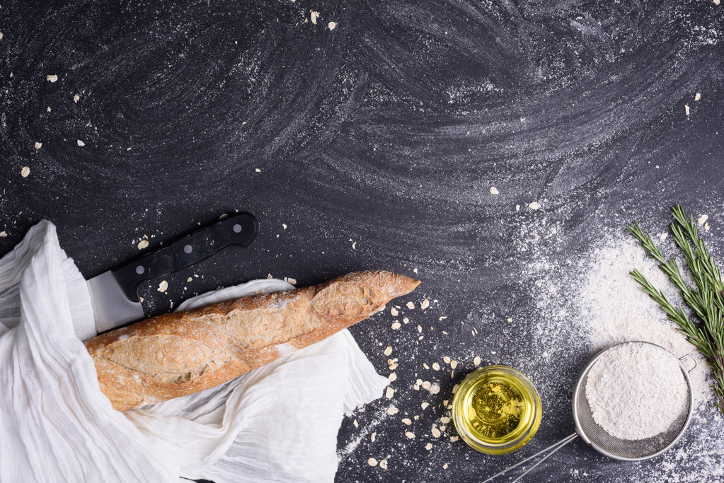 French baguette with ingredients: rosemary, olive oil, garlic, knife and flour over black grunge background. Top view, free text space. - Photo, Image